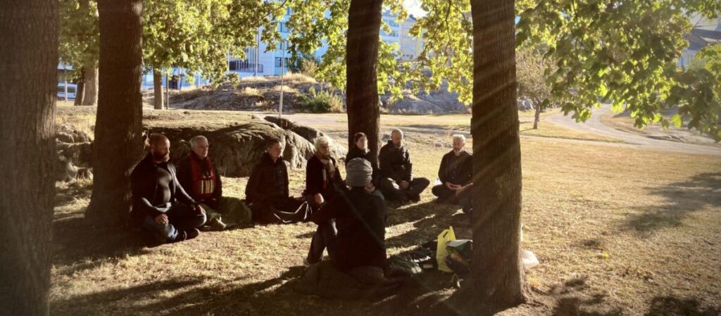 Kuvassa joukko ihmisiä meditoivat syyskuun kellertävässä aamuauringossa helsinkiläisessä puistossa